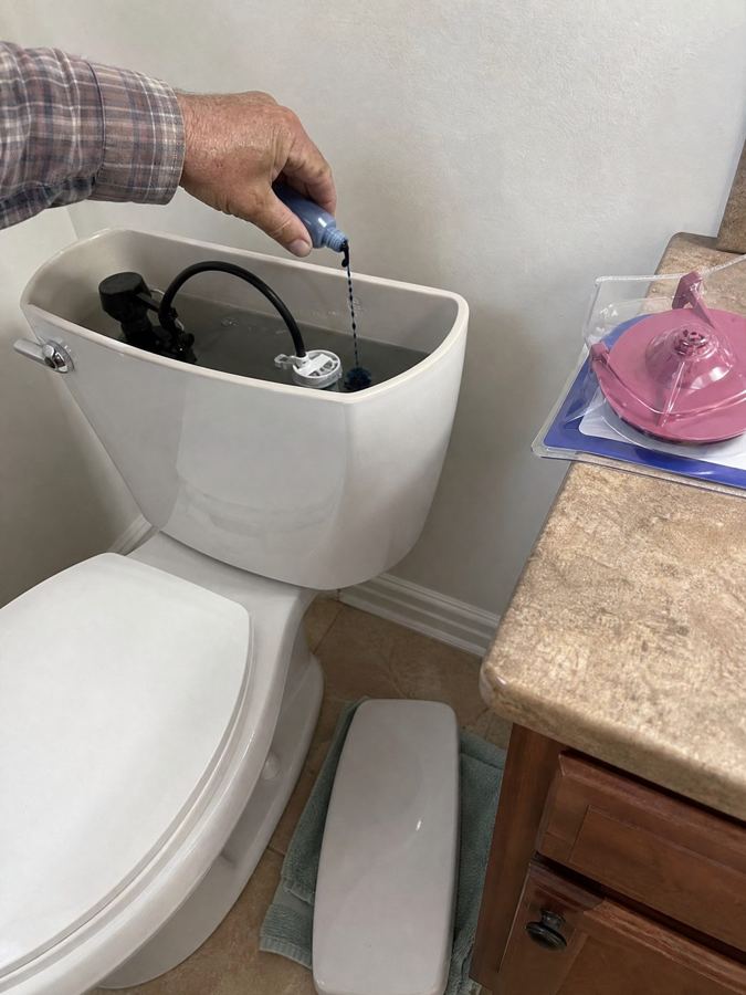 A hand dropping dye into a toilet tank